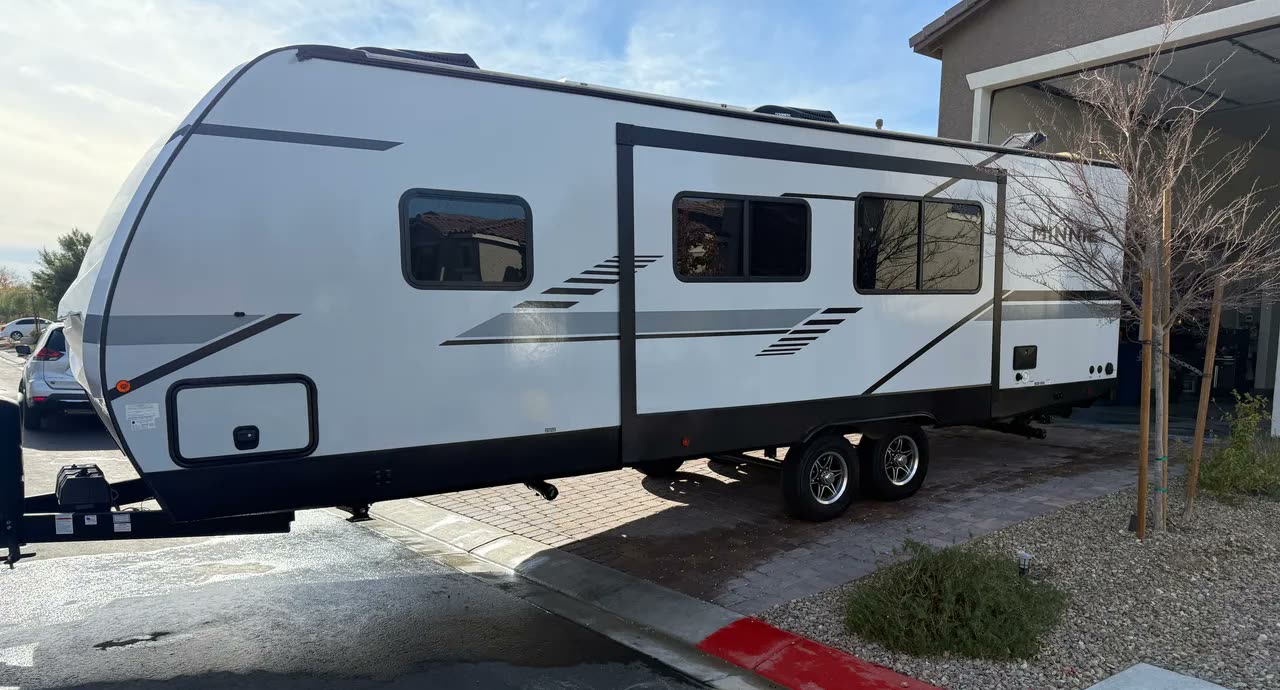 The House&rsquo;s travel trailer, a white Winnebago Minnie, hitched and ready on the driveway before the faire.